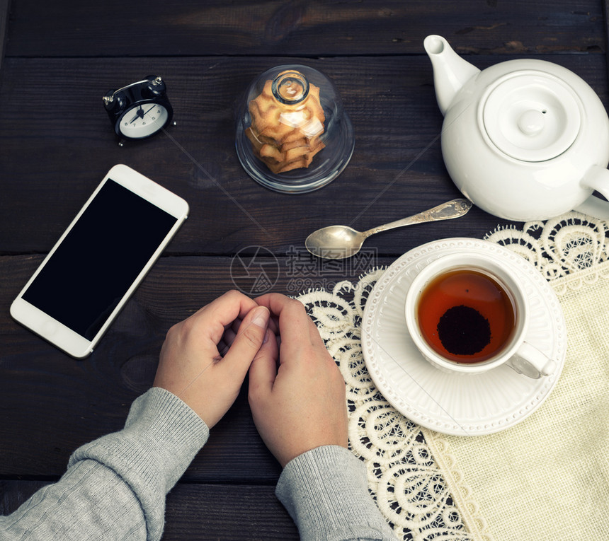 两只女手躺在木制桌子上旁边是茶杯和智能手机图片