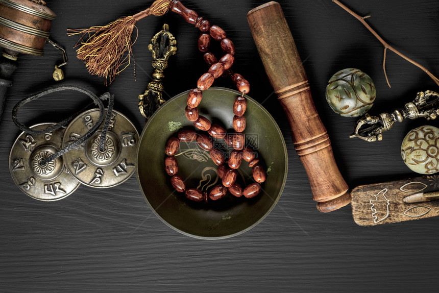 铜碗祈祷珠鼓石球和其他宗教物体用于在黑木背景下默思和替代药物顶视图片