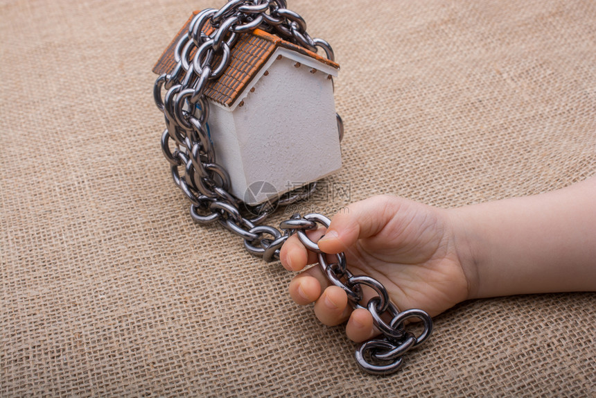 小手握着一条链环绕着棕色背景的模范房子图片