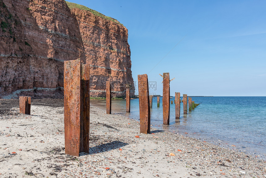 带有红悬崖和生锈铁柱的海边岛带有红悬崖和老旧破碎码头生锈铁柱的海边岛图片