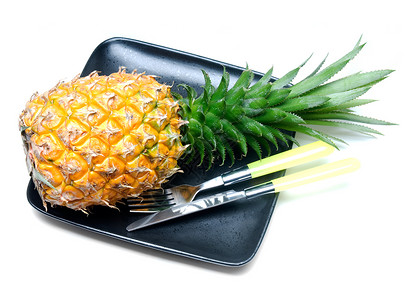 黄色黑色叉子黑色盘子上的熟菠萝用刀和叉子在白色上隔离背景