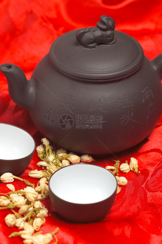 茶叶干鲜花罐子和两个杯红色丝绸桌布图片