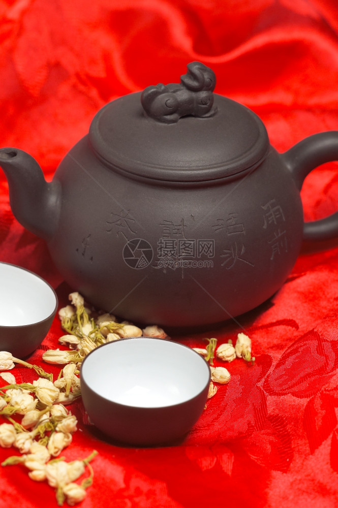茶叶干鲜花罐子和两个杯红色丝绸桌布图片