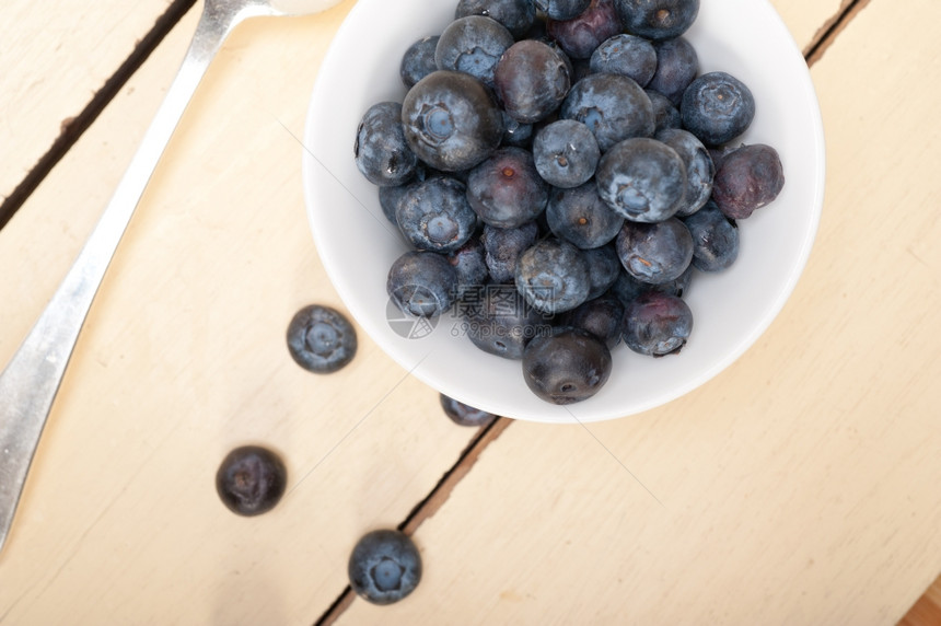 一碗新鲜的蓝莓边有银勺子放在木桌上图片