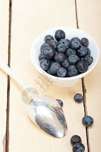 一碗蓝莓一碗新鲜的蓝莓边有银勺子放在木桌上背景