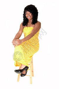 一个美丽的非裔国女人穿着长黄色的裙子黑头发坐在椅子上白背景图片