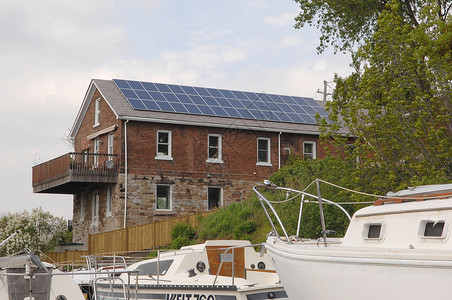 一座老房子屋顶上装有现代太阳能电池从中获取能源船头前方有帆图片