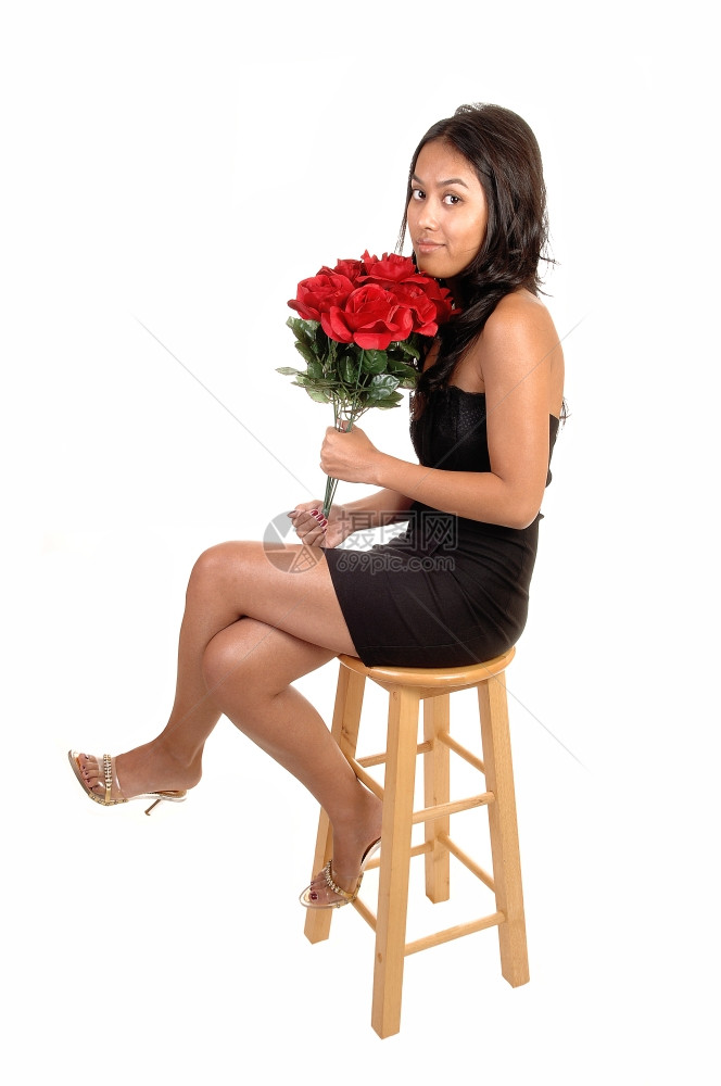 一个美丽又瘦的亚洲女人坐在椅子上手里拿着一堆红玫瑰穿着黑色的裙子和高跟鞋穿着白色的背景图片