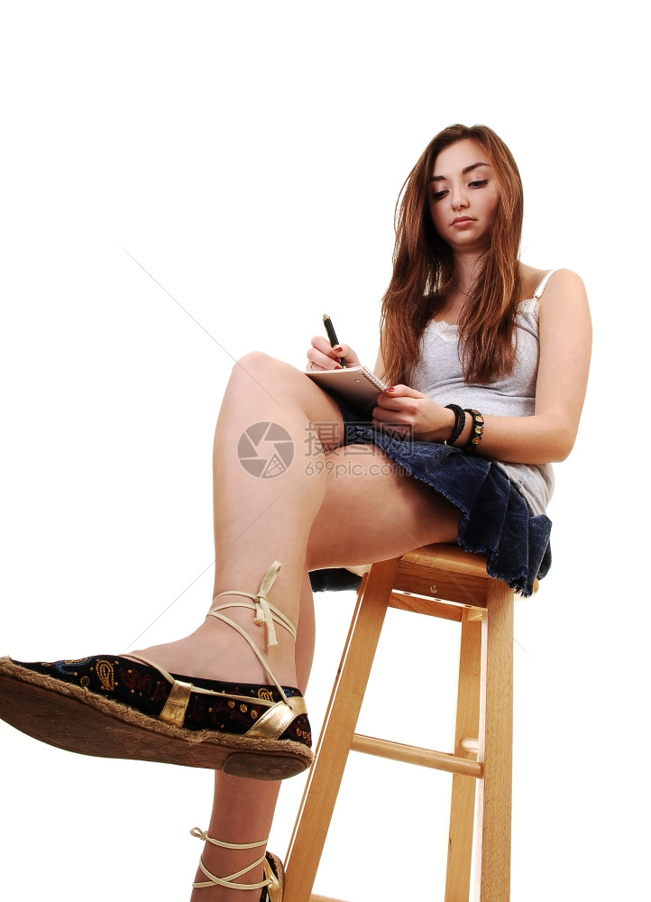 一个年轻的少坐在椅子上穿着裙长的黑发手里拿着一本笔记白背景图片