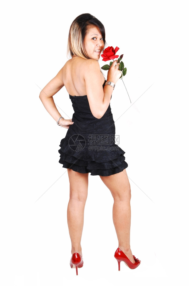 一个穿红色高跟鞋的年轻漂亮亚洲女人一条短的黑裙子手握着一朵红玫瑰背对着摄影机站图片