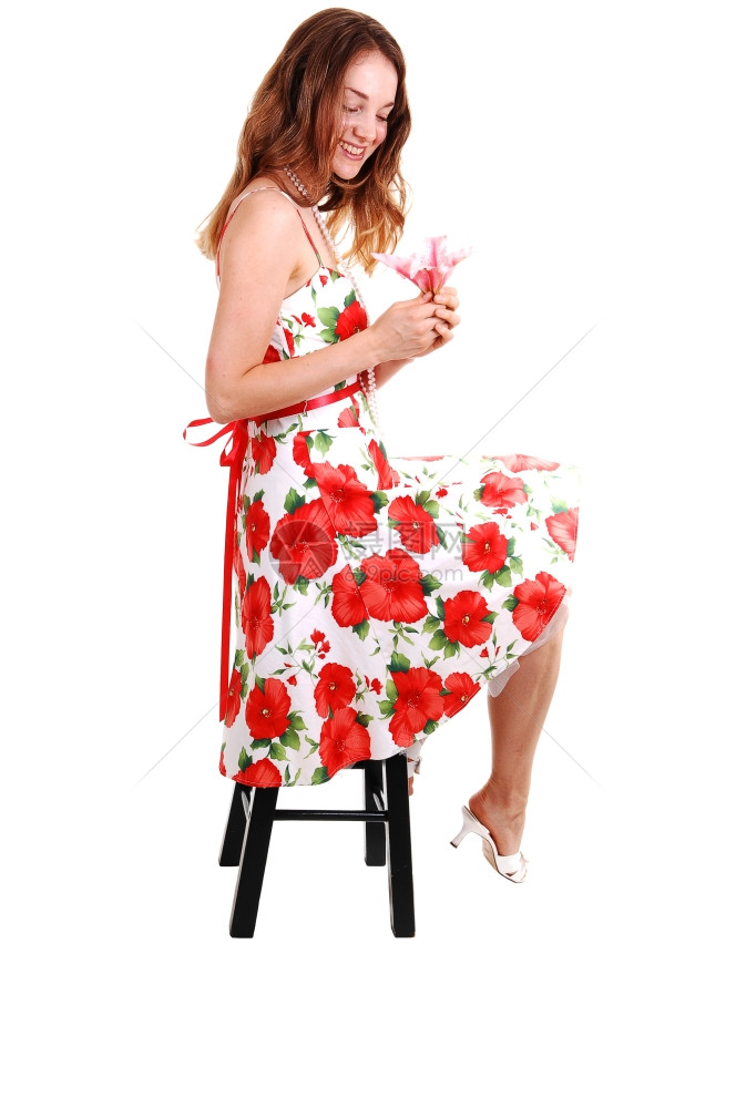 年轻可爱的姑娘穿着多彩的裙子棕发期待她的花在手中高跟鞋坐着工作室的白色背景图片