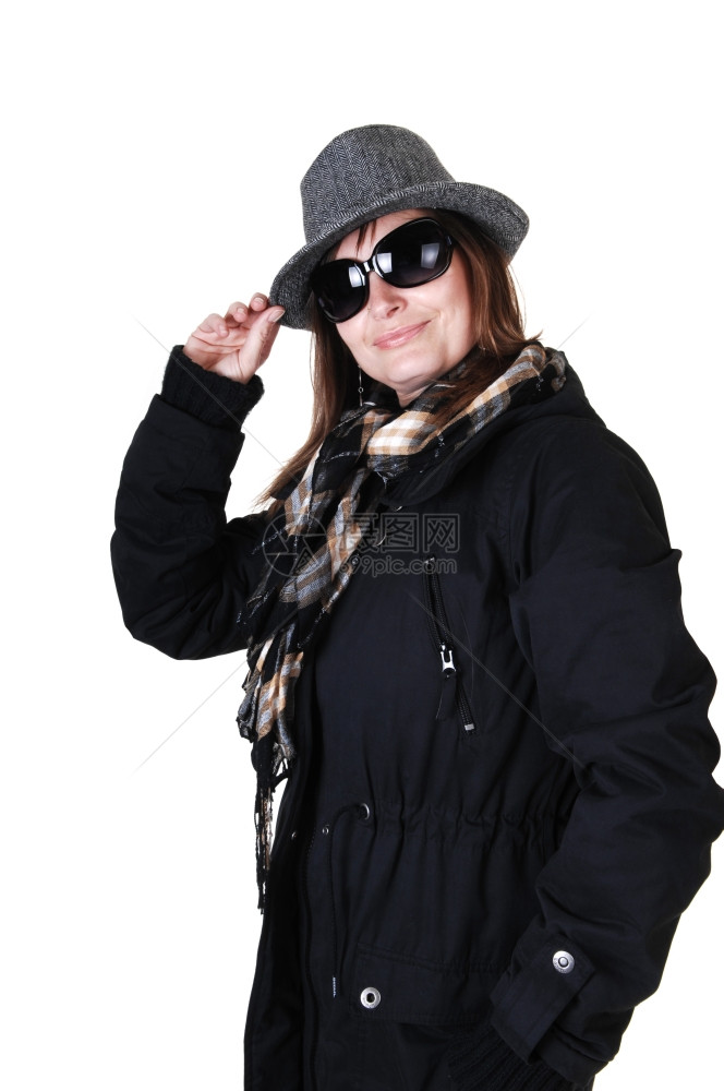 身穿深蓝色冬大衣棕靴和带墨镜围巾的海绵帽中年妇女站在工作室里寻找白背景图片
