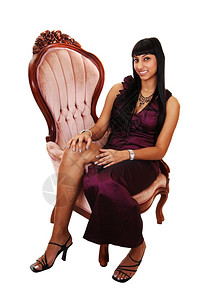 一位美丽的女人坐在长卷发裙里坐在抗粉红色的椅子上长黑头发落在肩上白的图片