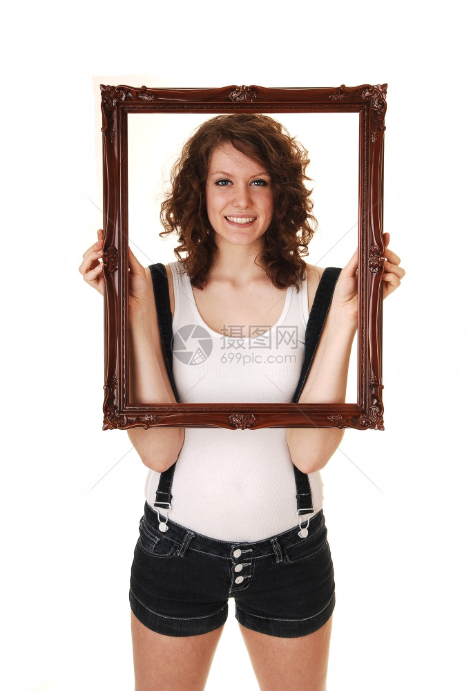 一个穿牛仔裤的年轻美女穿着吊带和白色T恤在工作室里拿着一个图片框白色背景图片