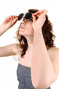 一位美丽的年轻女举起太阳镜检查它们是否干净白色背景图片