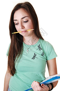 一个穿绿色T恤嘴里拿着铅笔的年轻美女长着黑发站在工作室里寻找白背景图片