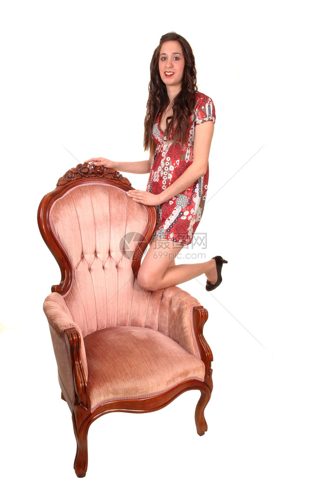 一个漂亮的女人站在工作室粉红色的椅子上穿着多彩的裙子微笑在相机图片