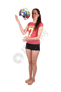 一个瘦的年轻女子站在工作室酒吧脚下玩着彩色足球黑短裤白背景图片