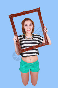 一个漂亮女孩拿着一个照片框头部跪在地板上穿绿短裤蓝色背景图片