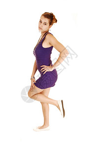 一个穿长裙子的漂亮年轻女抬起一条腿站在白背景上手放在臀部图片