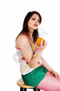一位年轻女坐在绿短裤和长袍上坐在椅子手里拿着黄色橙与白种背景隔绝图片