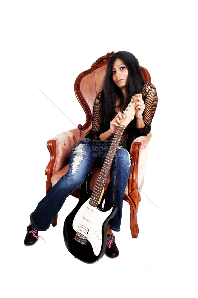 一位美丽的西班牙裔年轻女子拿着吉他坐在一张为白色背景而隔离的粉红色椅子上图片