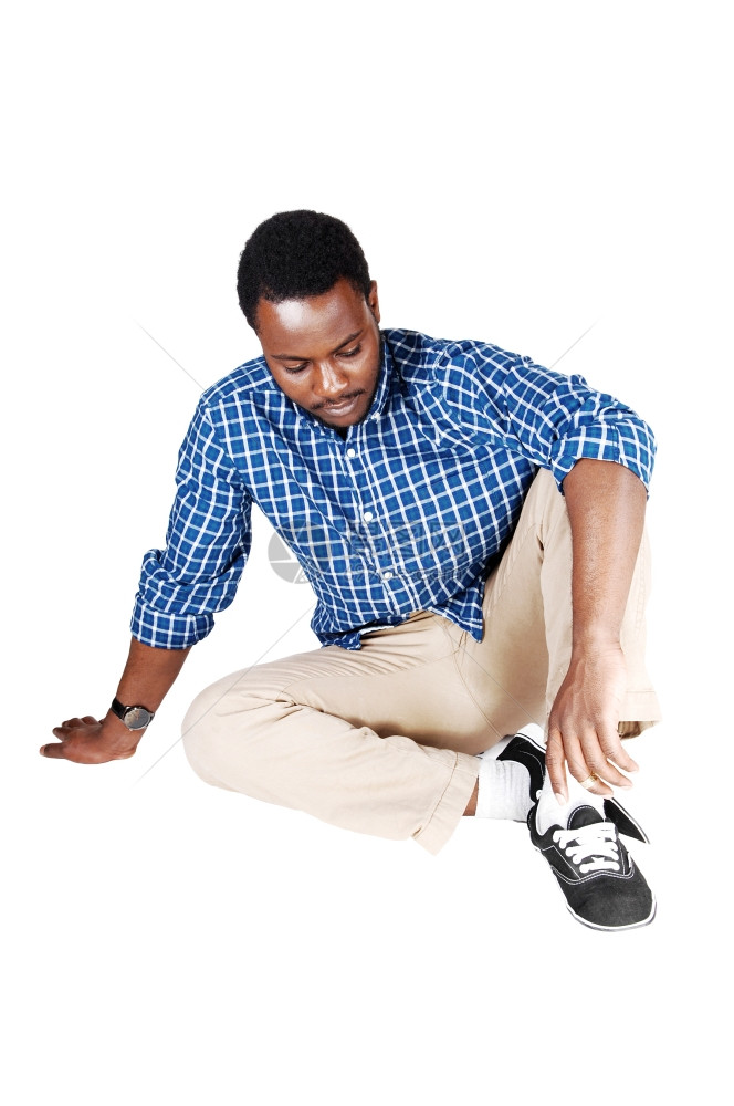 一个英俊的非裔美国人穿着米色裤子蓝衫坐在地板上被白色背景隔离图片