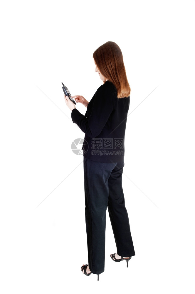 一个高瘦的年轻女商人站在背面的黑色西装电话里聊天与白背景隔绝图片