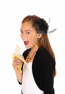 一个可爱的年轻女孩站在一个特写图片隔离为白后方张开嘴吃香蕉图片