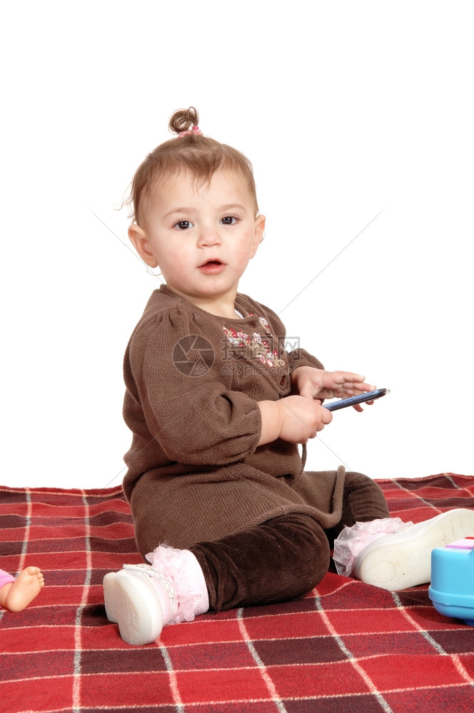 一个穿着棕色裙子的漂亮女婴坐在地板上的毯子白背景孤立无援图片