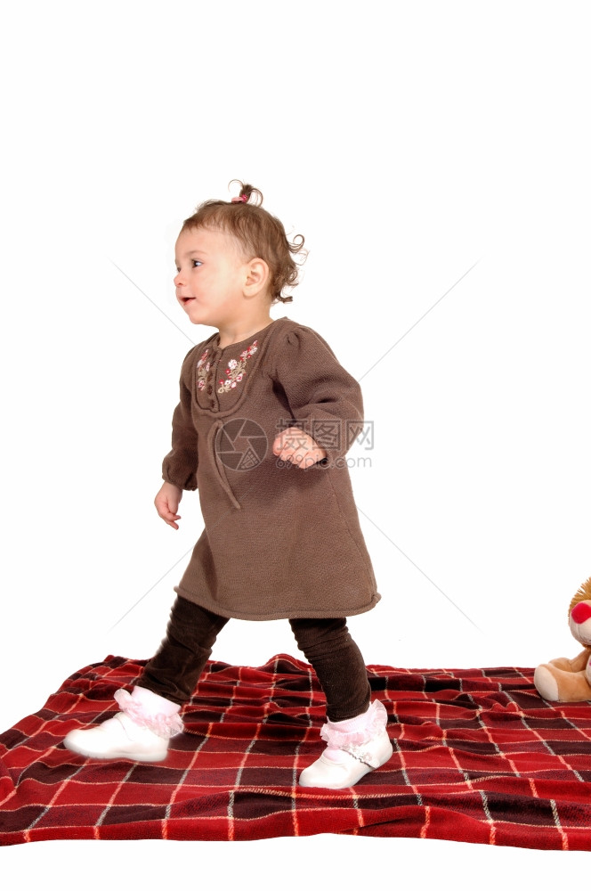 一个穿着棕色裙子的小女孩穿着毛毯在地板上行走为了白色背景而孤立无援图片