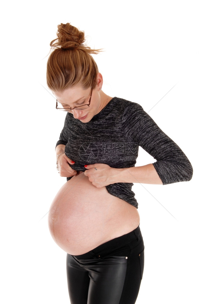 一个高怀孕的女士抬起她衣服看着大肚子孤立白色背景图片