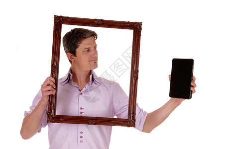 一个年轻男子拿着一个图片框看着他平板上的深处孤立白色背景图片