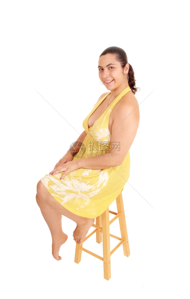 一个微笑着的年轻女人穿着黄色的裙子坐在工作室里椅子上微笑着与白种背景隔绝图片