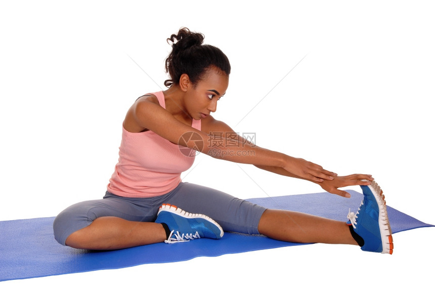 一个年轻的美国女孩坐在瑜伽垫子上伸展身体为了健康与白种背景隔绝图片