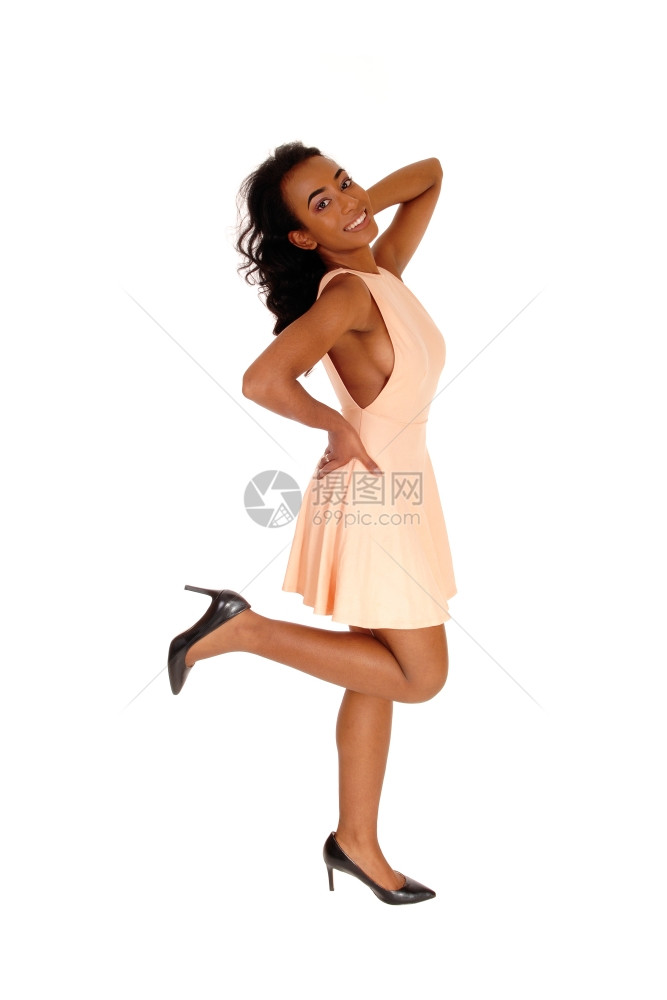 一个非洲裔的美国妇女站在一条腿上穿着米色洋装与白人背景隔绝图片