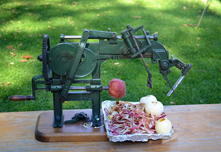 一个非常老旧的古董苹果剥皮机坐在桌子上有三个剥皮的苹果还有一个在工作图片