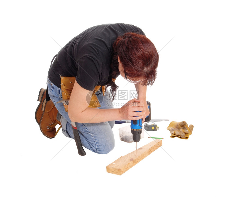 一名中年妇女跪在地上用一些工具在木头中钻探为白色背景而隔离图片