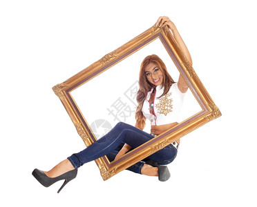 一位美丽的年轻女子坐在牛仔裤里一条腿穿过个画框与白色背景隔绝图片