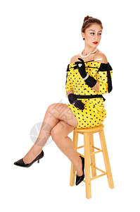 一位穿着黄色裙子的年轻美女拿着长烟筒坐在椅子上与白种背景隔绝背景图片