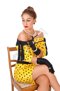 一位穿着黄色裙子的年轻美女拿着长烟筒坐在椅子上望着一而去与白种背景隔绝背景图片