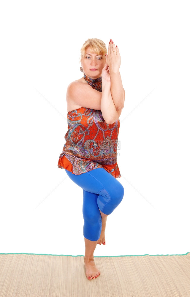 一个美丽的金发女人站在地板上展示一些漂亮的瑜伽穿着蓝裤与白背景隔绝图片