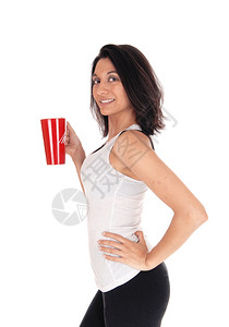 一个快乐笑容的年轻女子穿着白色T恤早上拿着红色咖啡卷与白背景隔绝图片