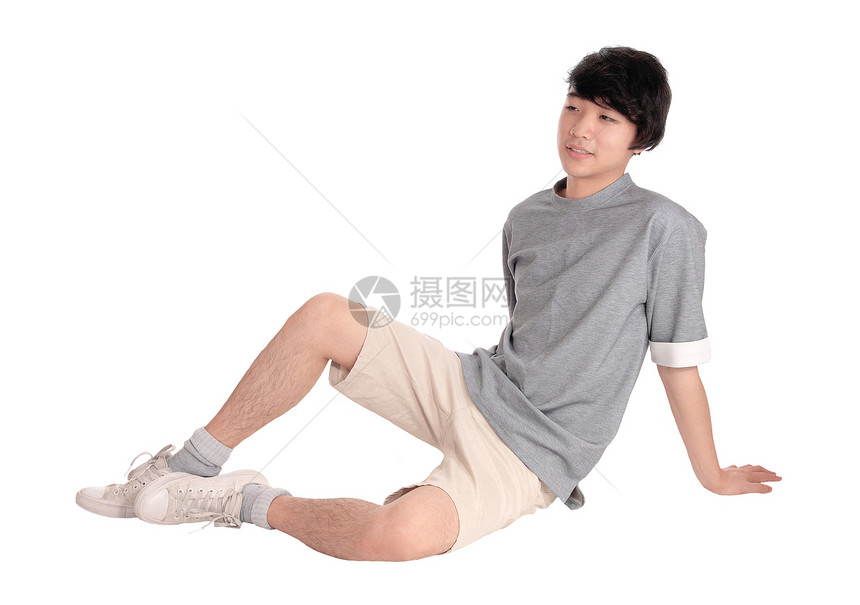 一个英俊漂亮的年轻亚洲青少坐在地板上微笑与白种背景隔绝图片