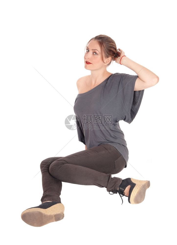 一个穿着牛仔裤和黑发的漂亮年轻女子坐在地上仰望着与白背景隔绝图片
