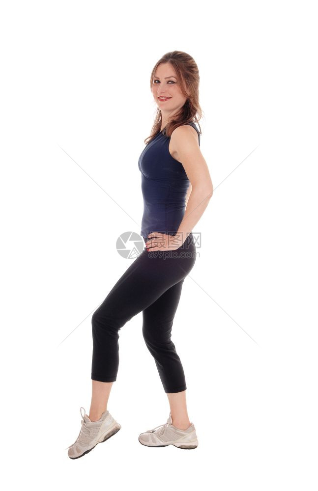 一个穿着运动服的美丽年轻女子站在白后地手伸臀部侧面图片