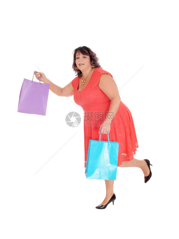 一名穿着红裙子的妇女拿着购物袋和高跟鞋因白种背景被隔离图片