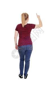 一个瘦的年轻女人站在牛仔裤和从背面穿布根迪毛衣从背后用一根手指向个图片