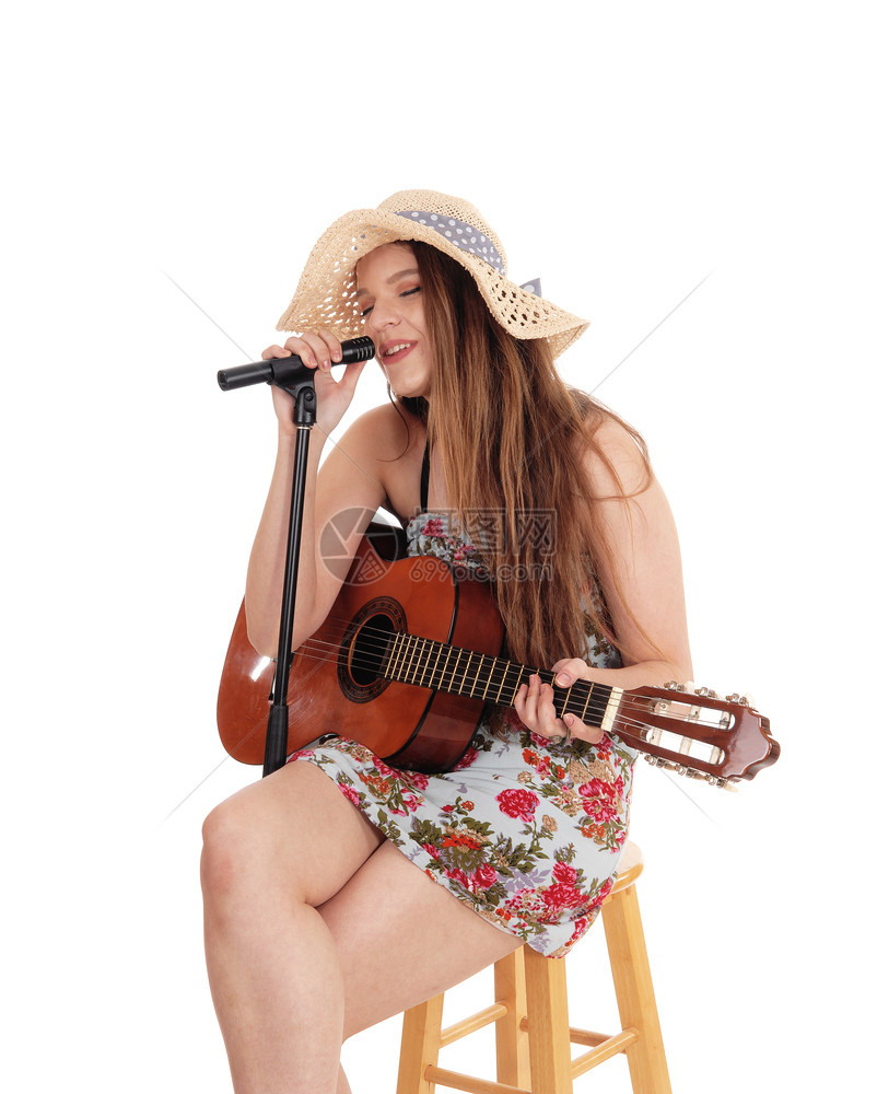 一个穿着多彩裙子的美女穿着草帽的玩吉他唱着麦克风与白背景隔绝图片