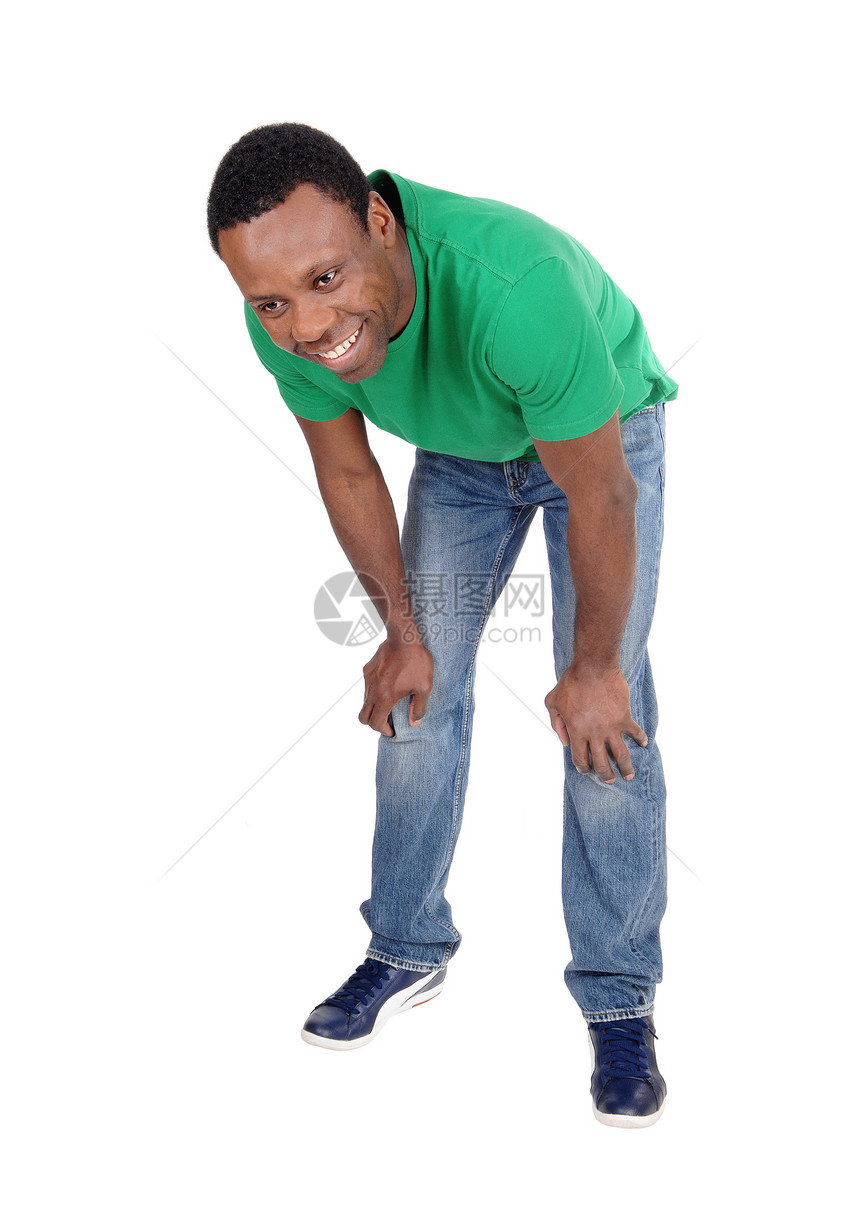 一个快乐笑的非裔美国人站在绿色马球衬衫和牛仔裤弯腰向前孤立于白背景图片